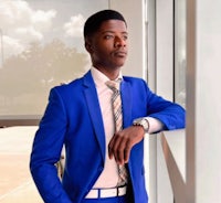 a young man in a blue suit leaning against a window